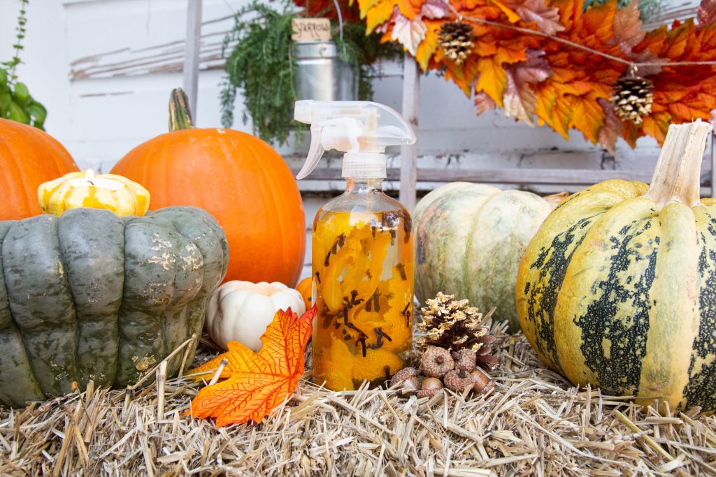 DIY fall cleaning spray with various colored gourds and a fall leaf garland sitting on a hay bale