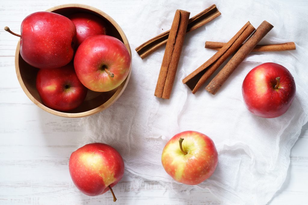 red apples and cinnamon sticks on a white surface