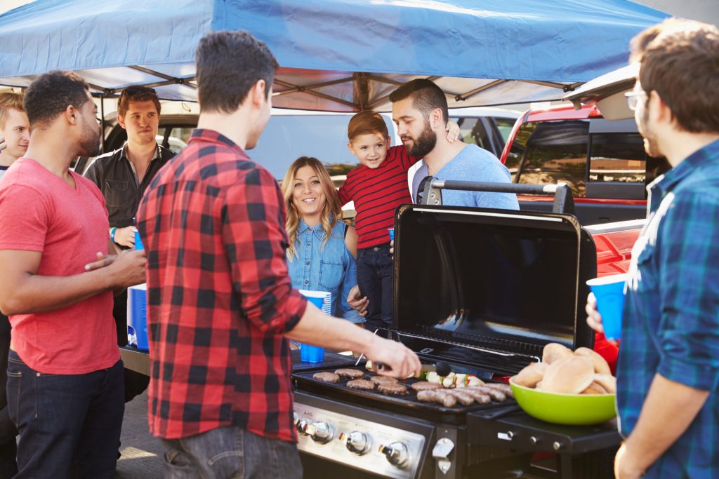 group gathered around a grill at a football tailgate