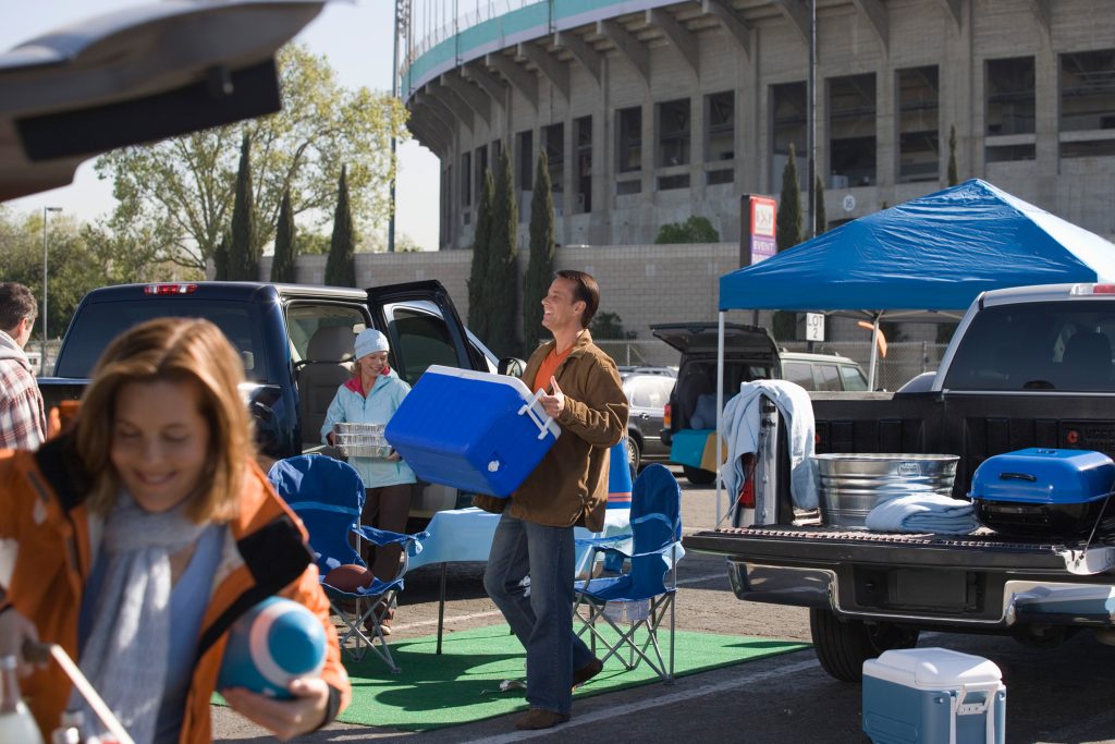 man carrying cooler setting up for a football tailgate