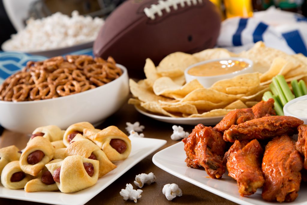 buffalo wings, pigs in a blanket, pretzels, queso and chips on a table