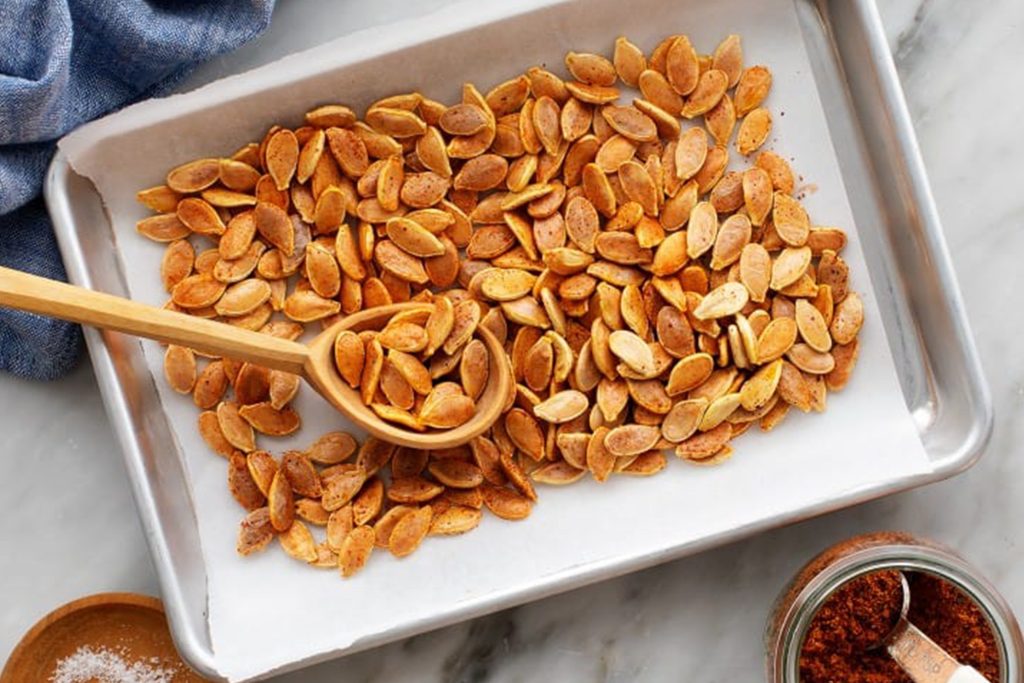 roasted pumpkin seeds on a baking sheet with parchment paper with seasonings next to the baking sheet