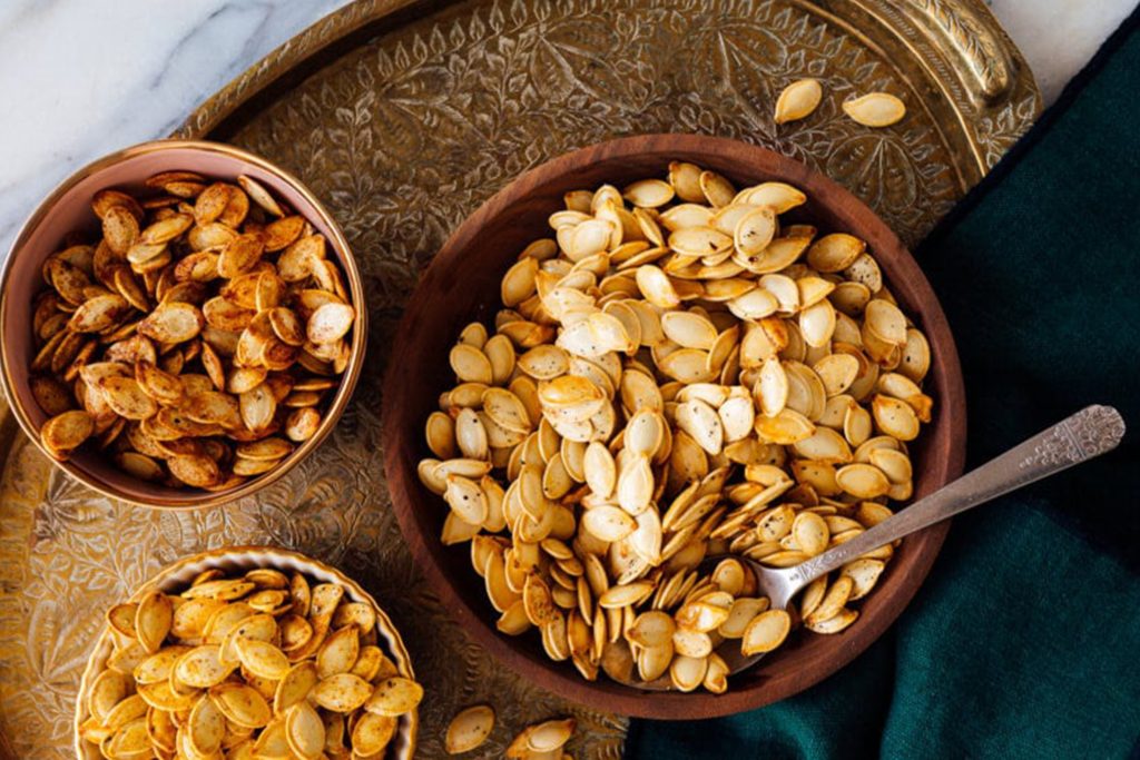 three bowls of different types of roasted pumpkin seeds on a brass serving platter