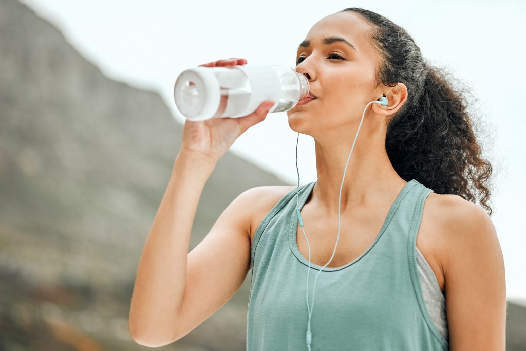 Woman with headphones drinking water from a bottle.