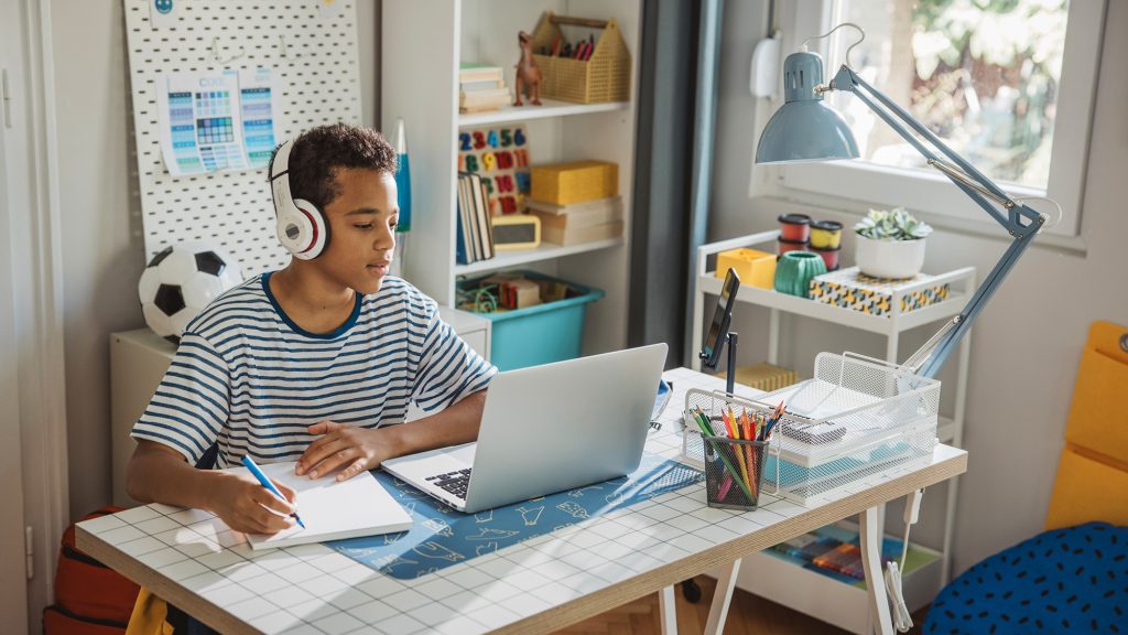 Kid working at a desk with a computer and notepad.
