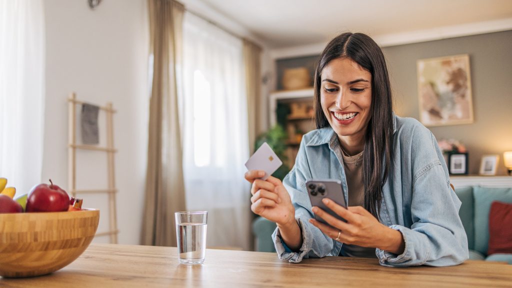 Woman sitting at table holding phone and credit card.