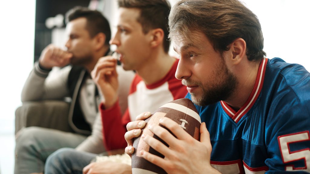 Three men watching football and one is holding a football.