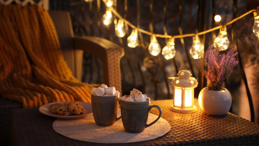 Hot chocolate on a patio table with string lights in the back.