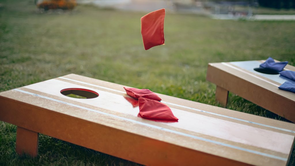 Bean bag being thrown at a corn hole board.