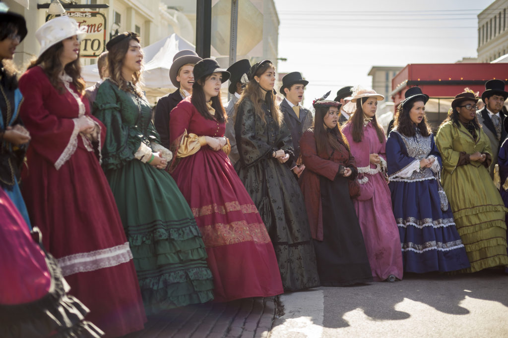 Group of people caroling in Victorian-era clothes.