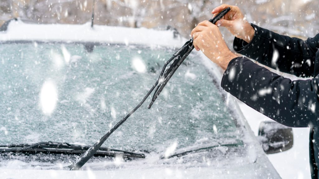 Person lifting windshield wipers of car during snow.