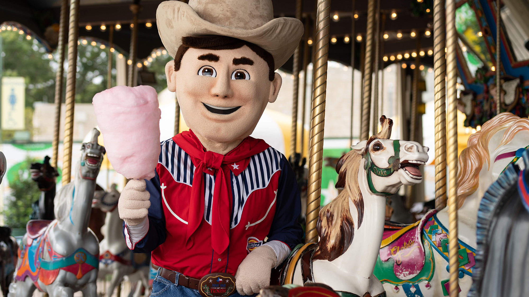 Mascot of Big Tex riding a carousel and holding cotton candy.
