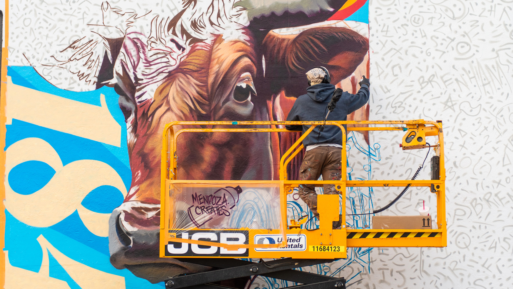 Man painting a large mural of a cow at an art festival.