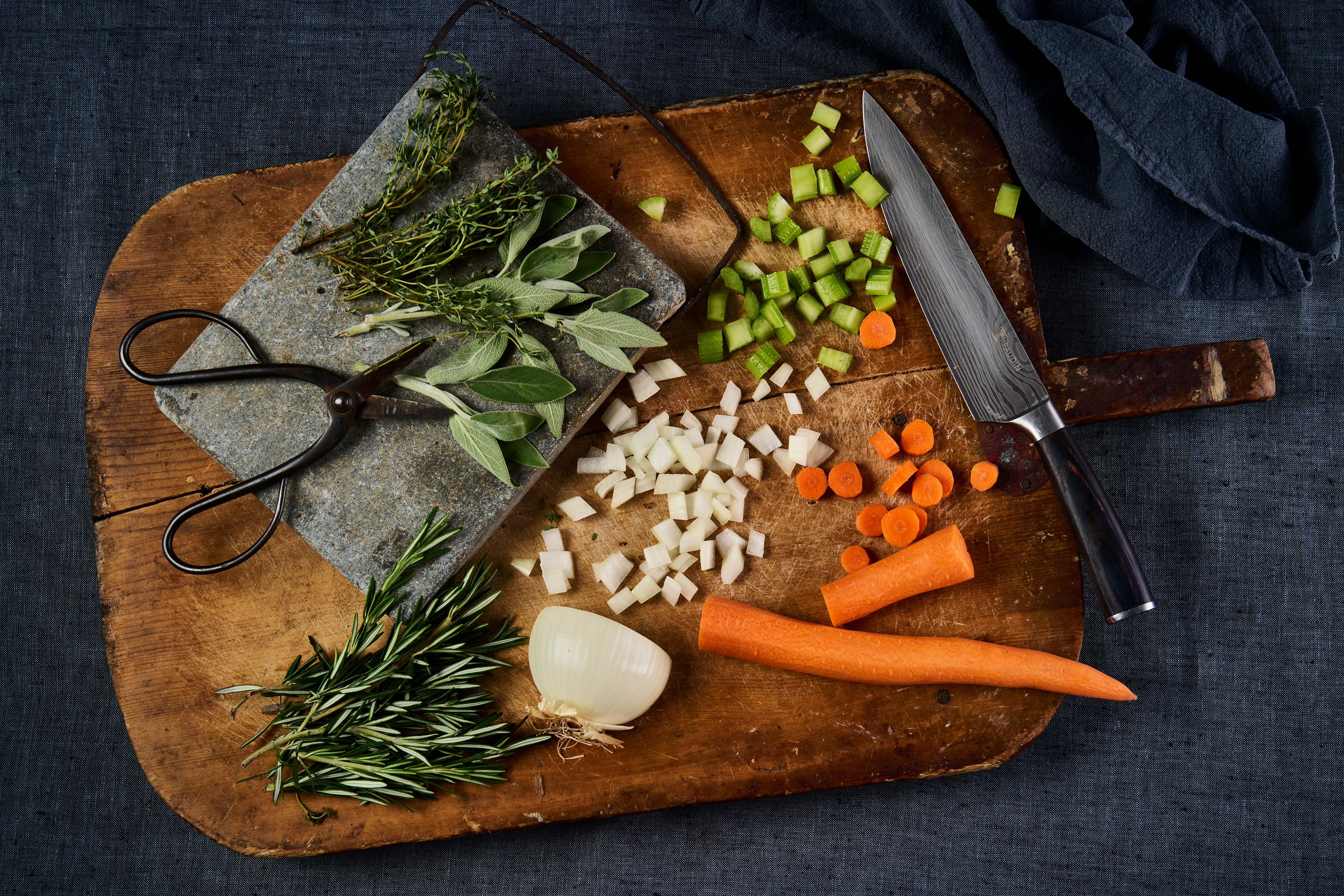 vegetables and herbs chopped on a distressed cutting board on a dark blue tablecloth