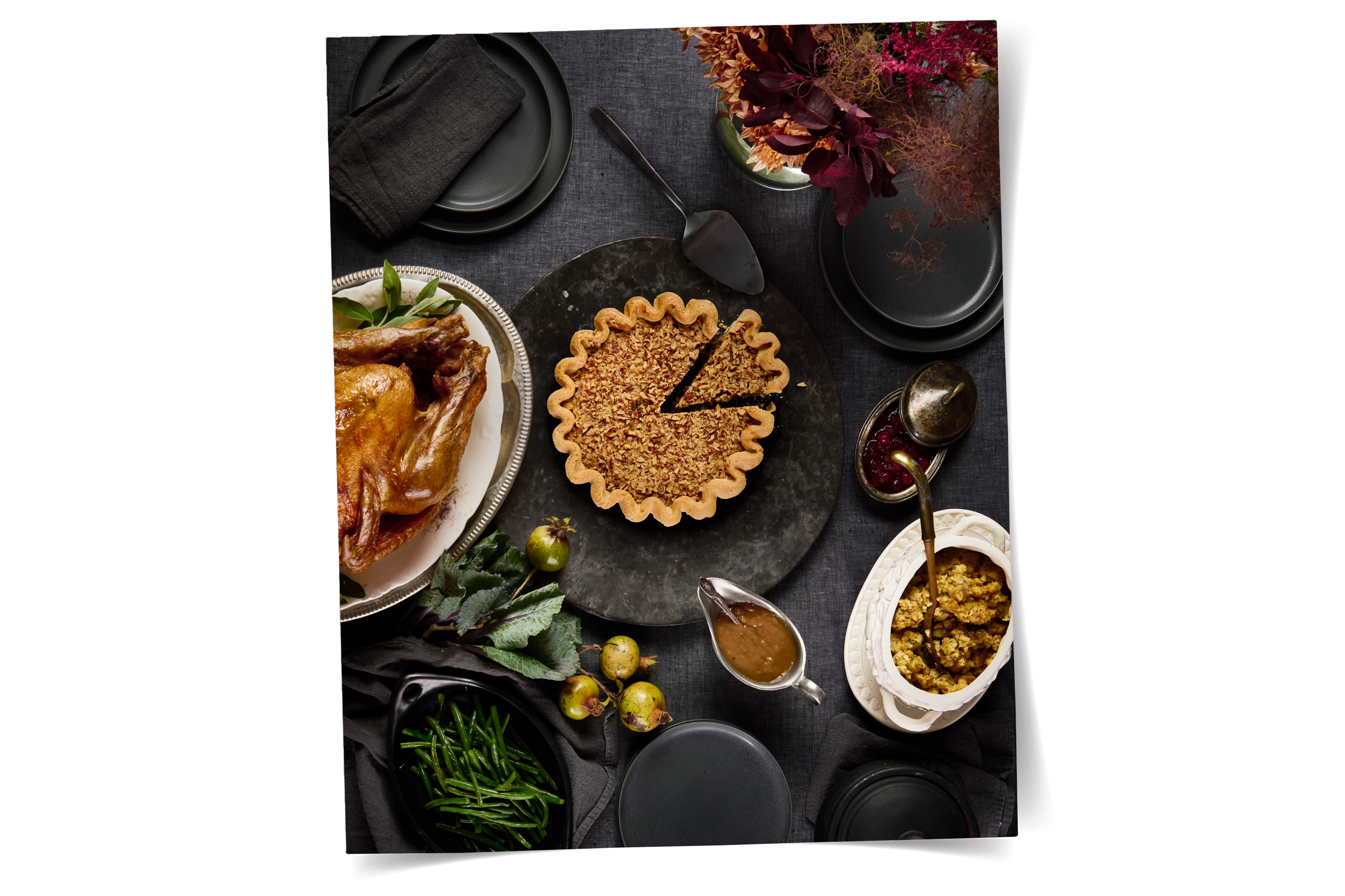 thanksgiving tablescape with a pecan pie, turkey, dressing, gravy, cranberries, green beans, plates, and floral arrangement 
