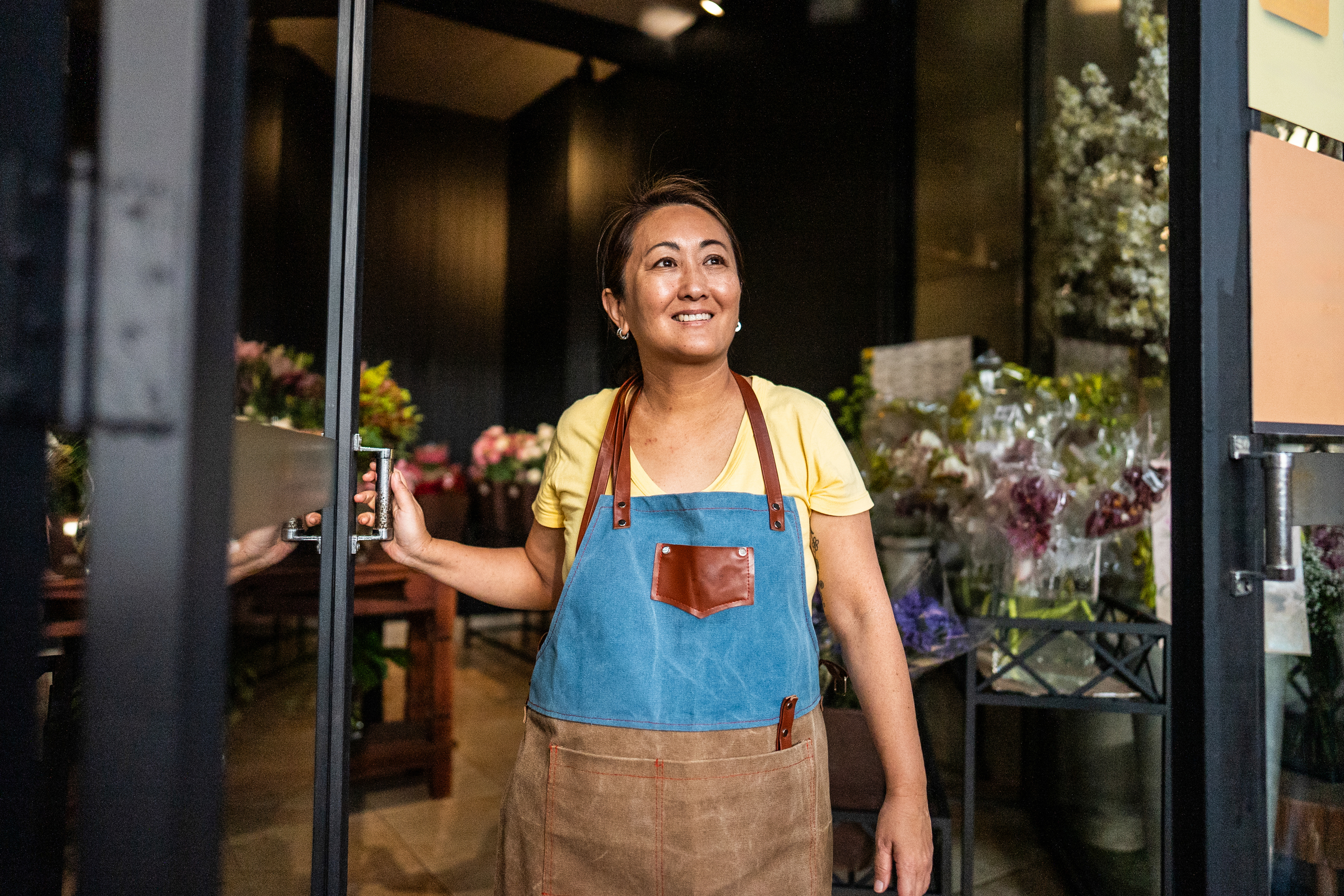 Woman holding door open to flower shop.