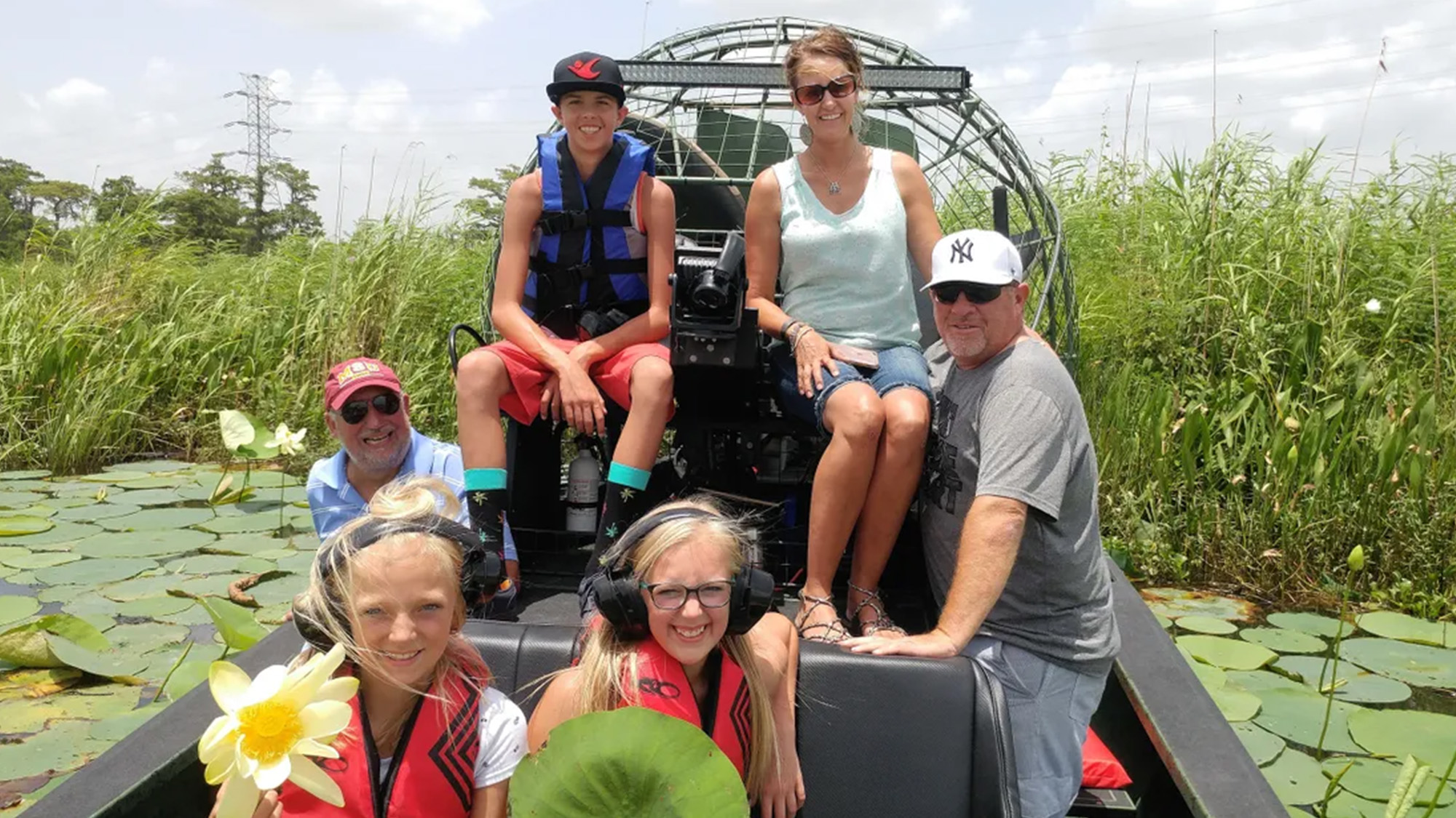 Group of people sitting in an air boat on the water surrounded by big lily pads.