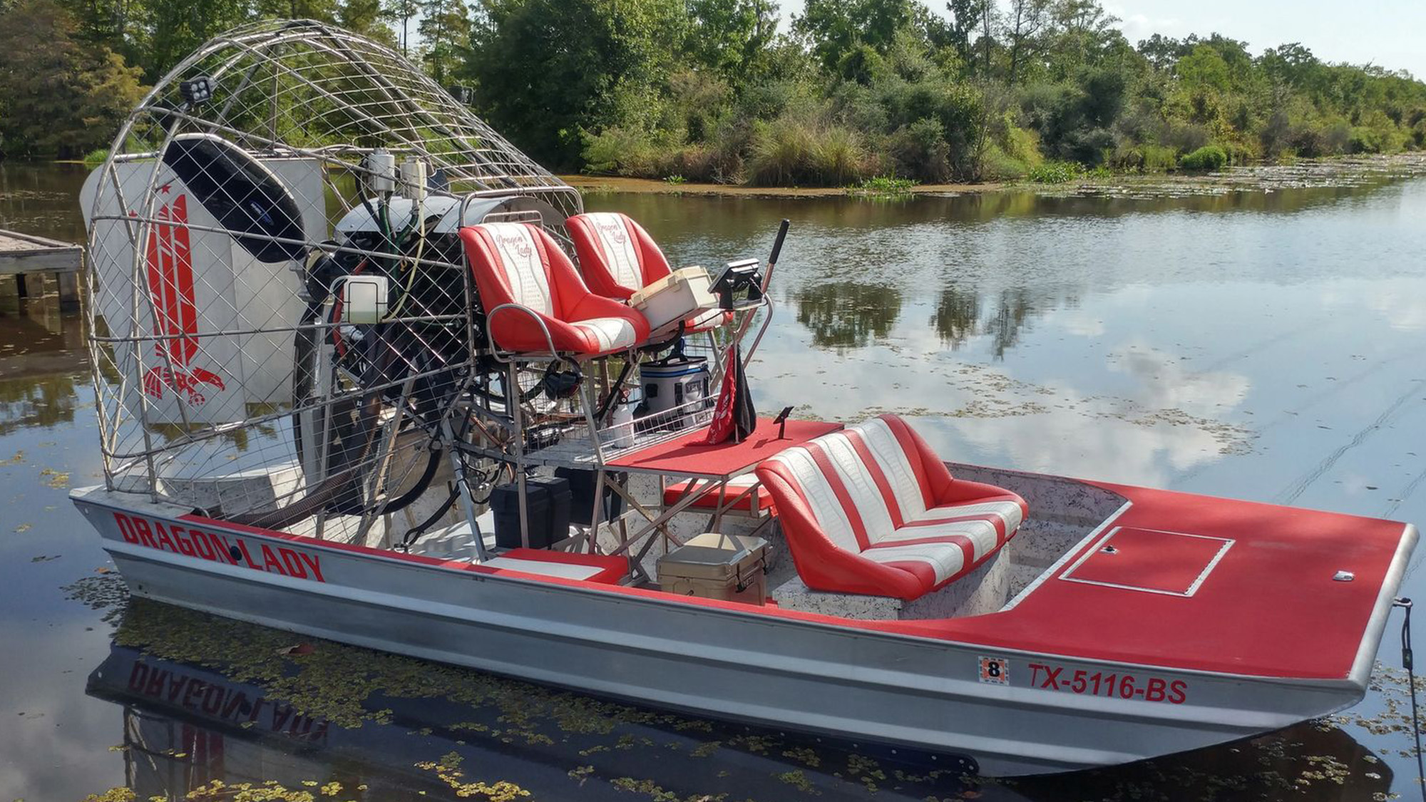 Dragon Lady red and white airboat docked on water.