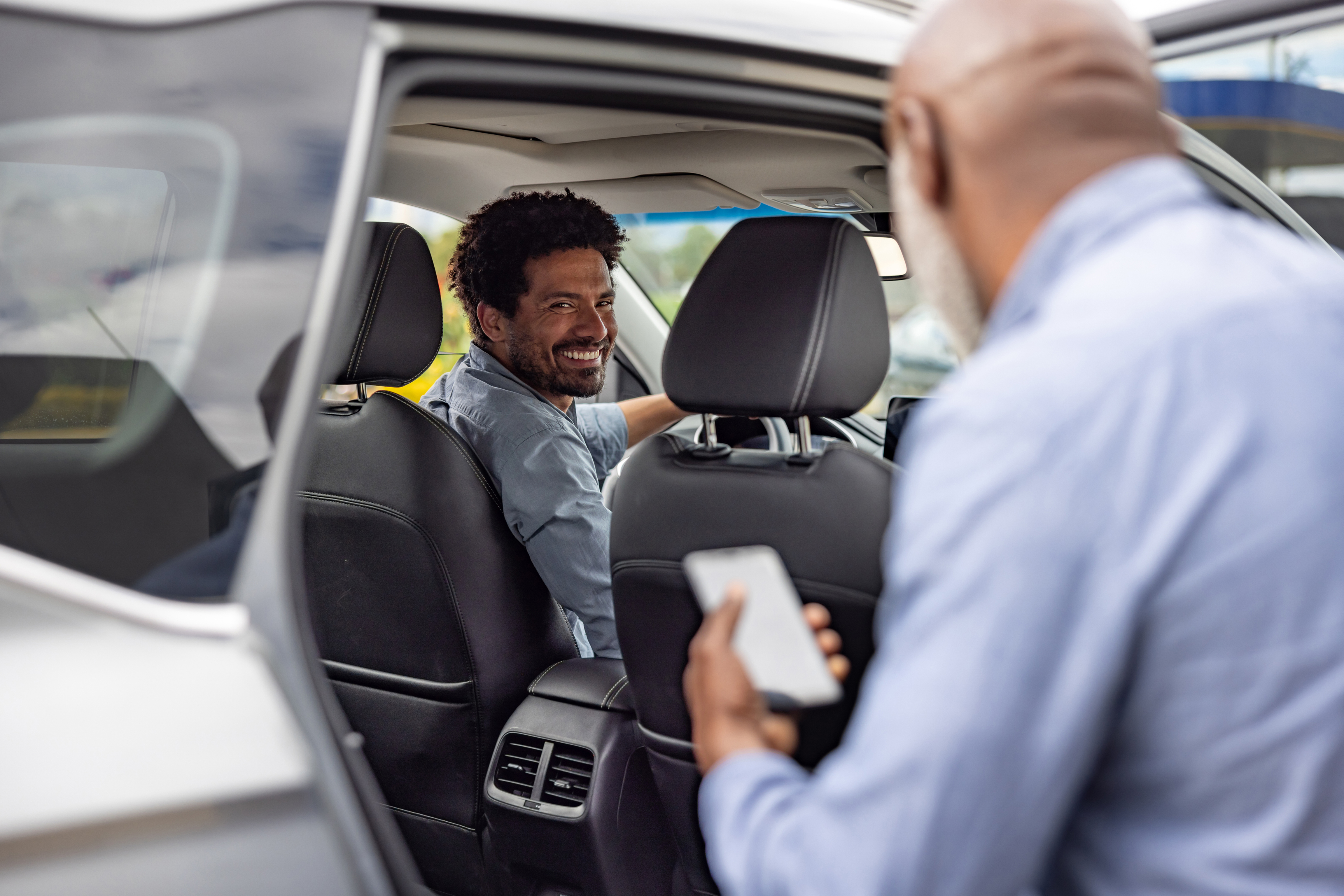 Man holding phone getting into car with man in driver's seat.