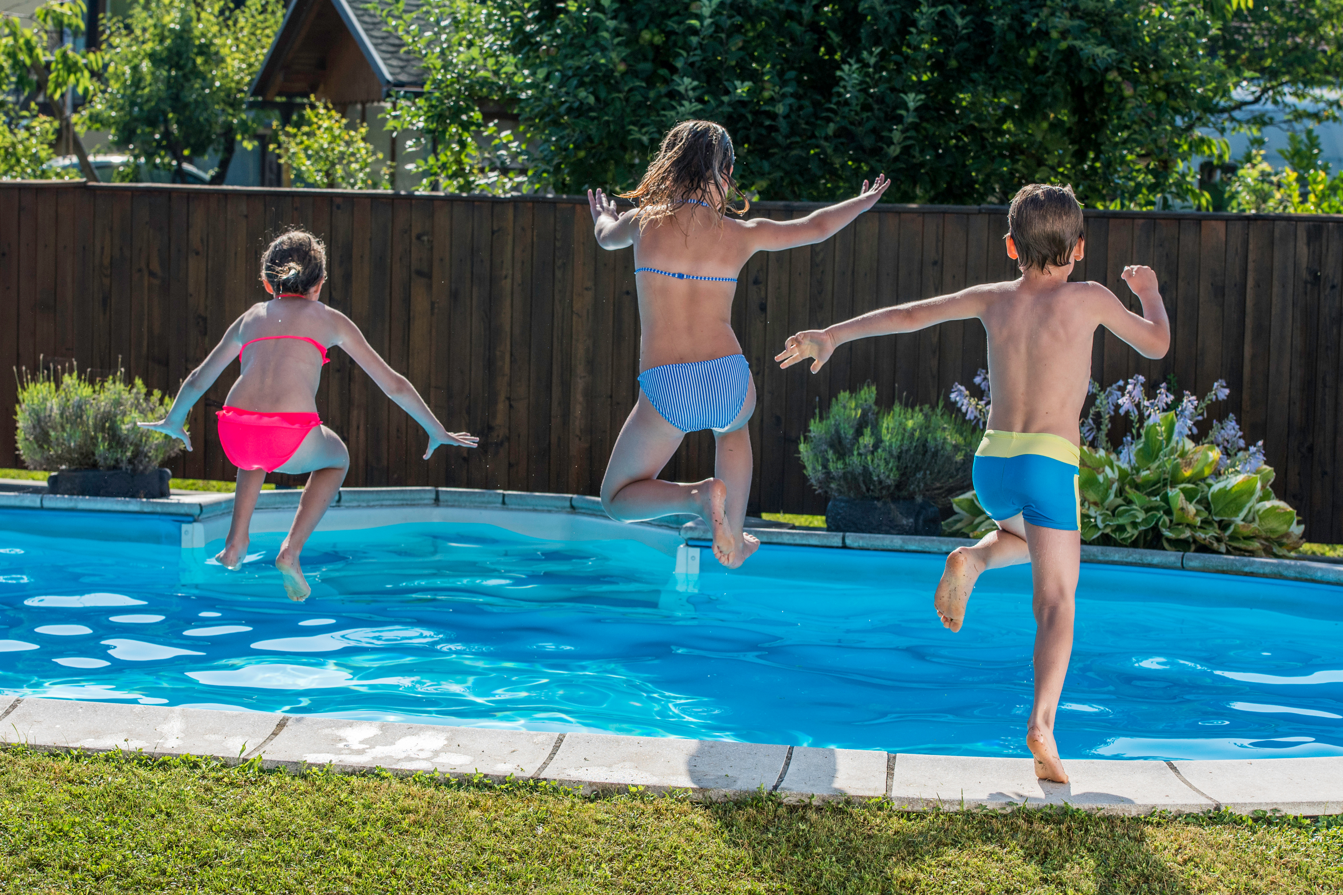 Three kids jumping into a pool.