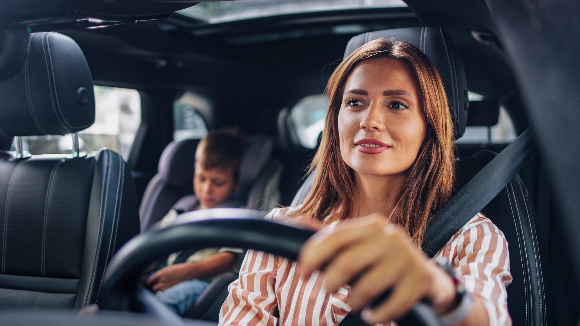 Woman driving car with kid in carseat in the back.