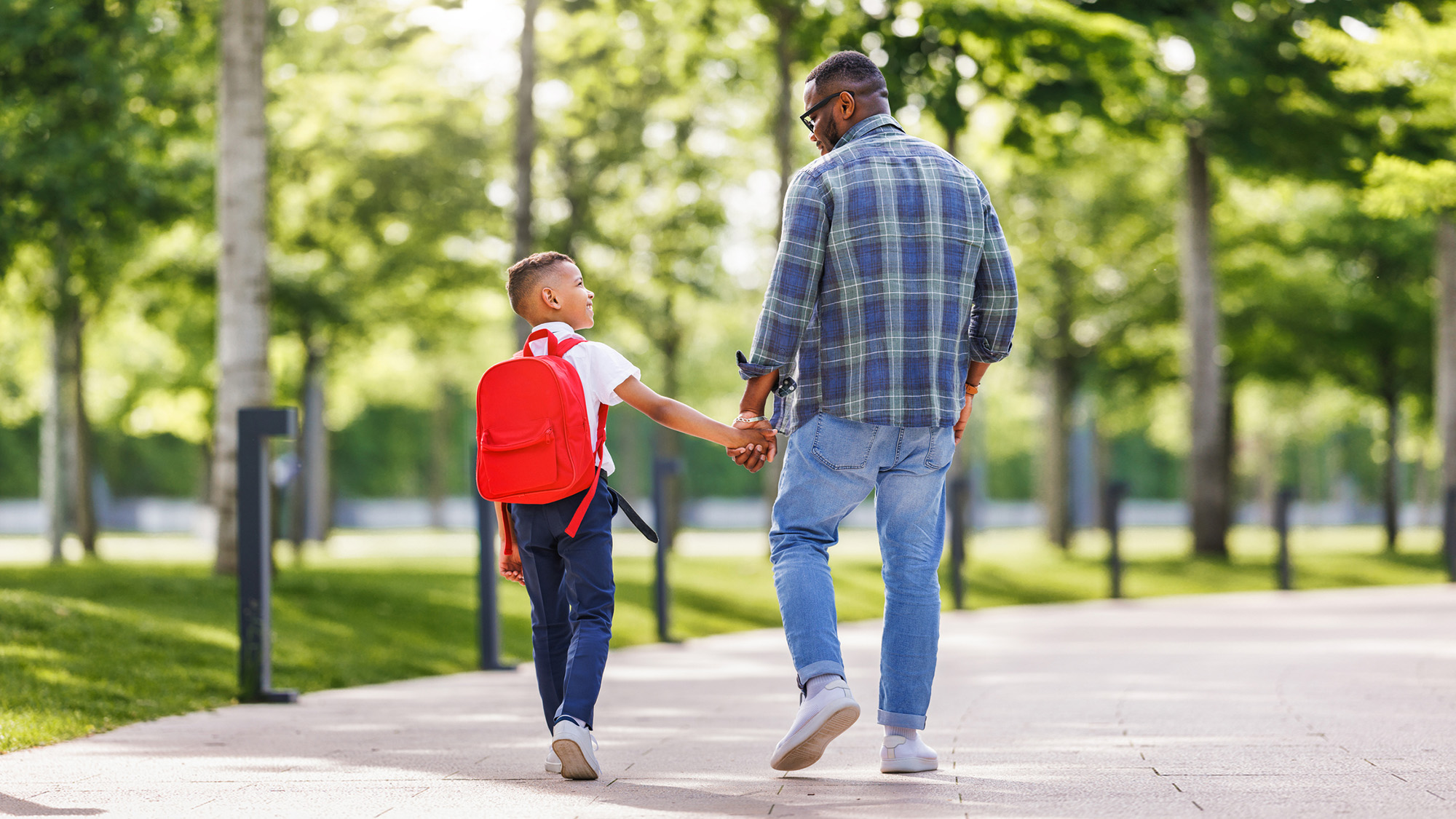 Man walking with young boy with a red backpack.