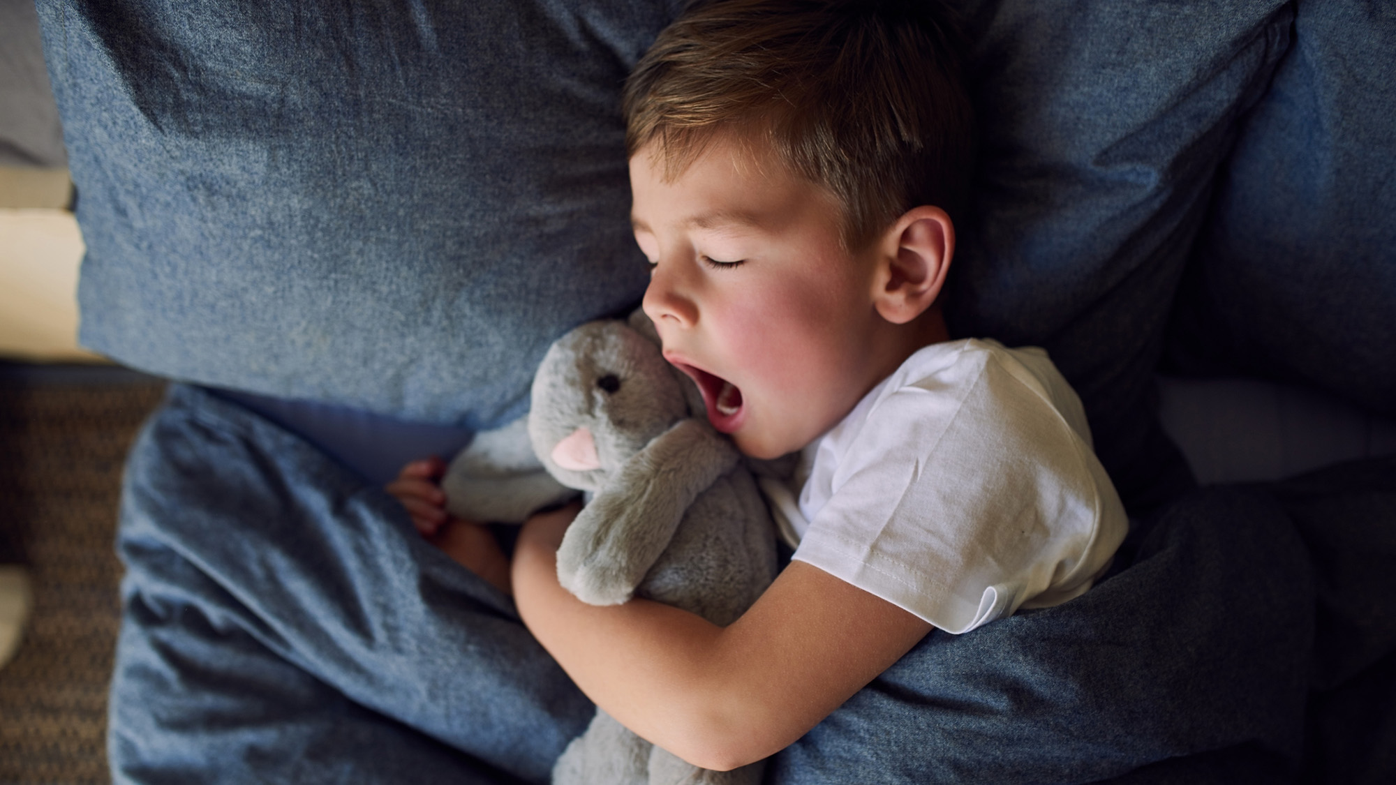 Kid waking up in bed with stuffed bunny toy.