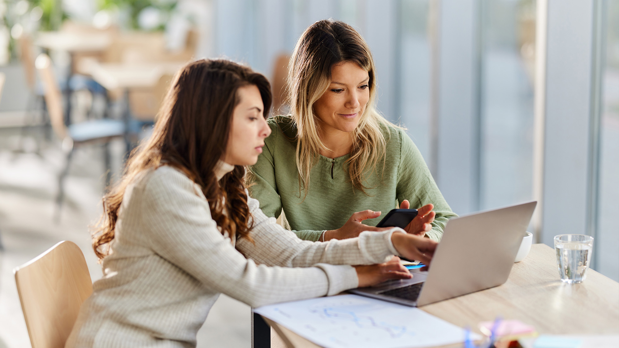 Two women sitting at a table working on a computer.