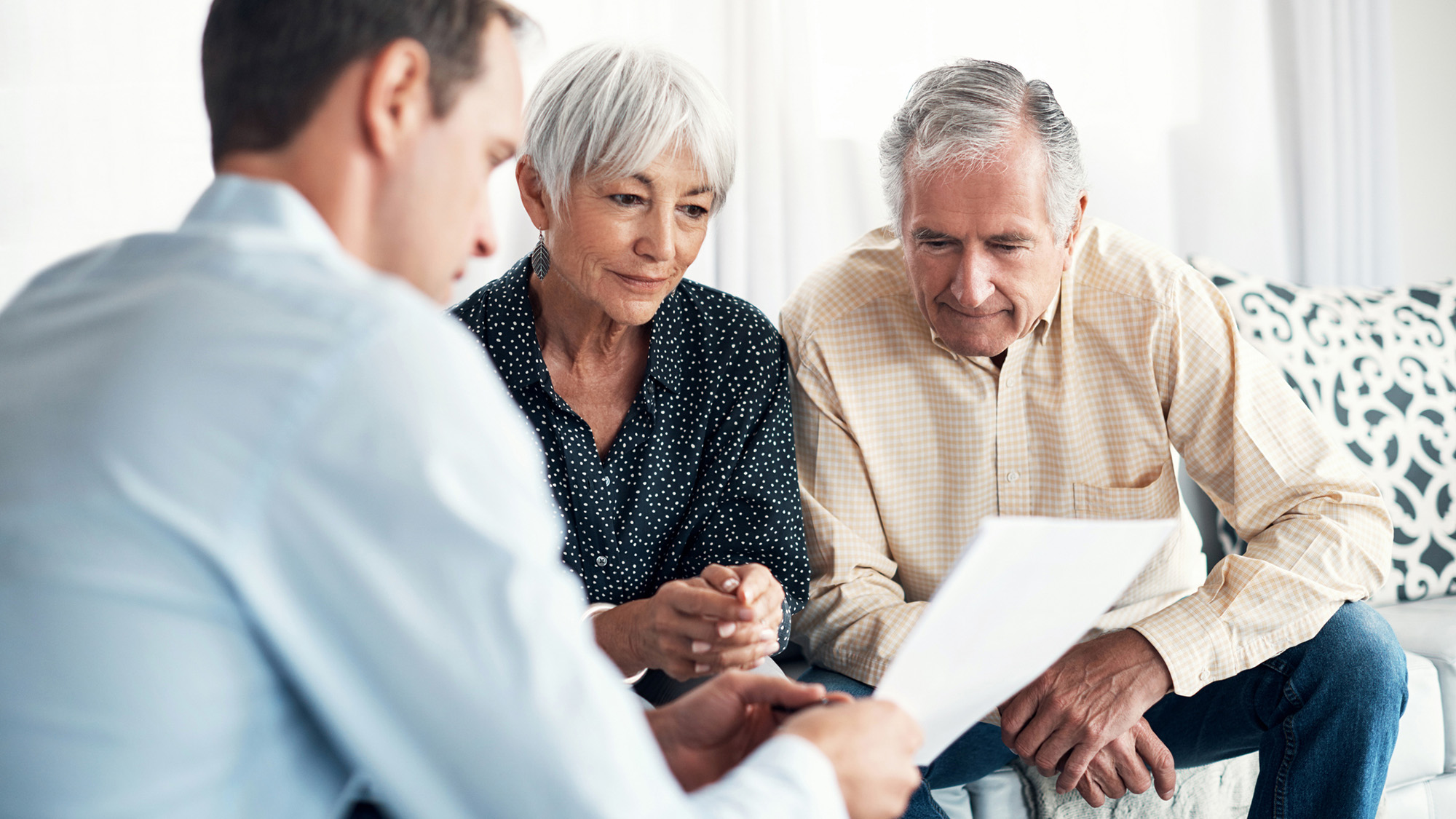 Man explaining something to man and woman on the couch.