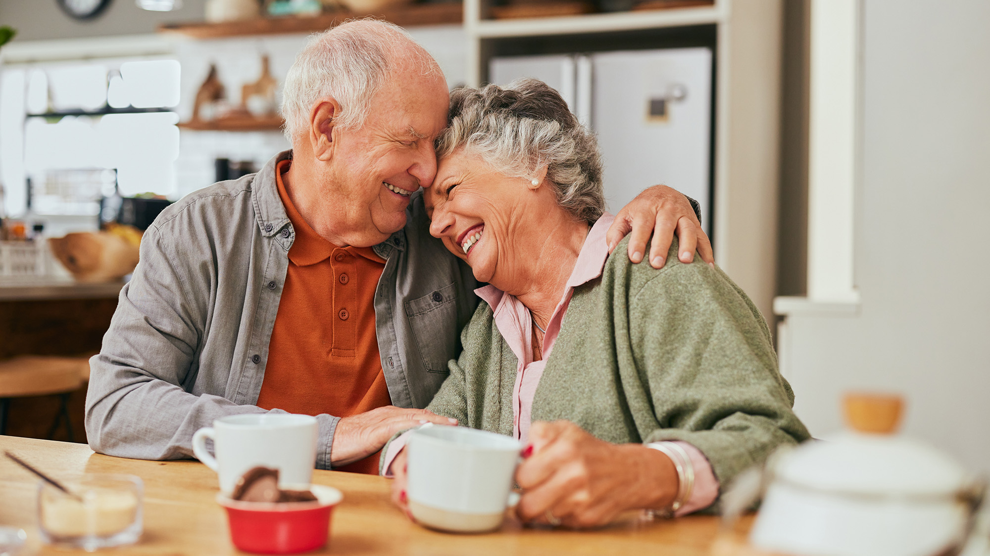 Older man and woman hugging at a table.