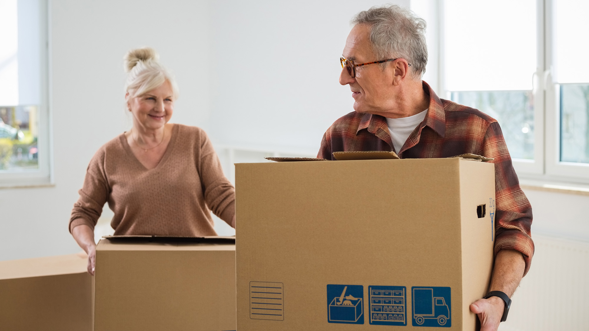Older man and woman carrying cardboard boxes.