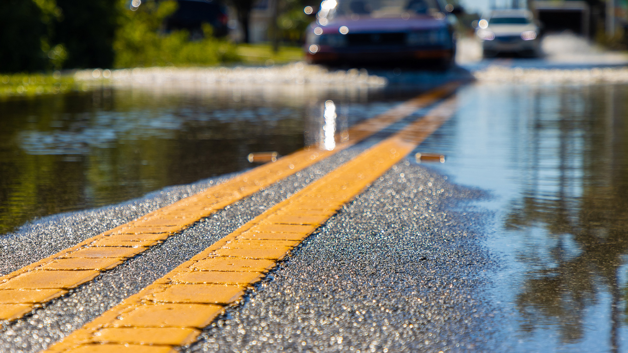 Flooded road with cars driving through water.
