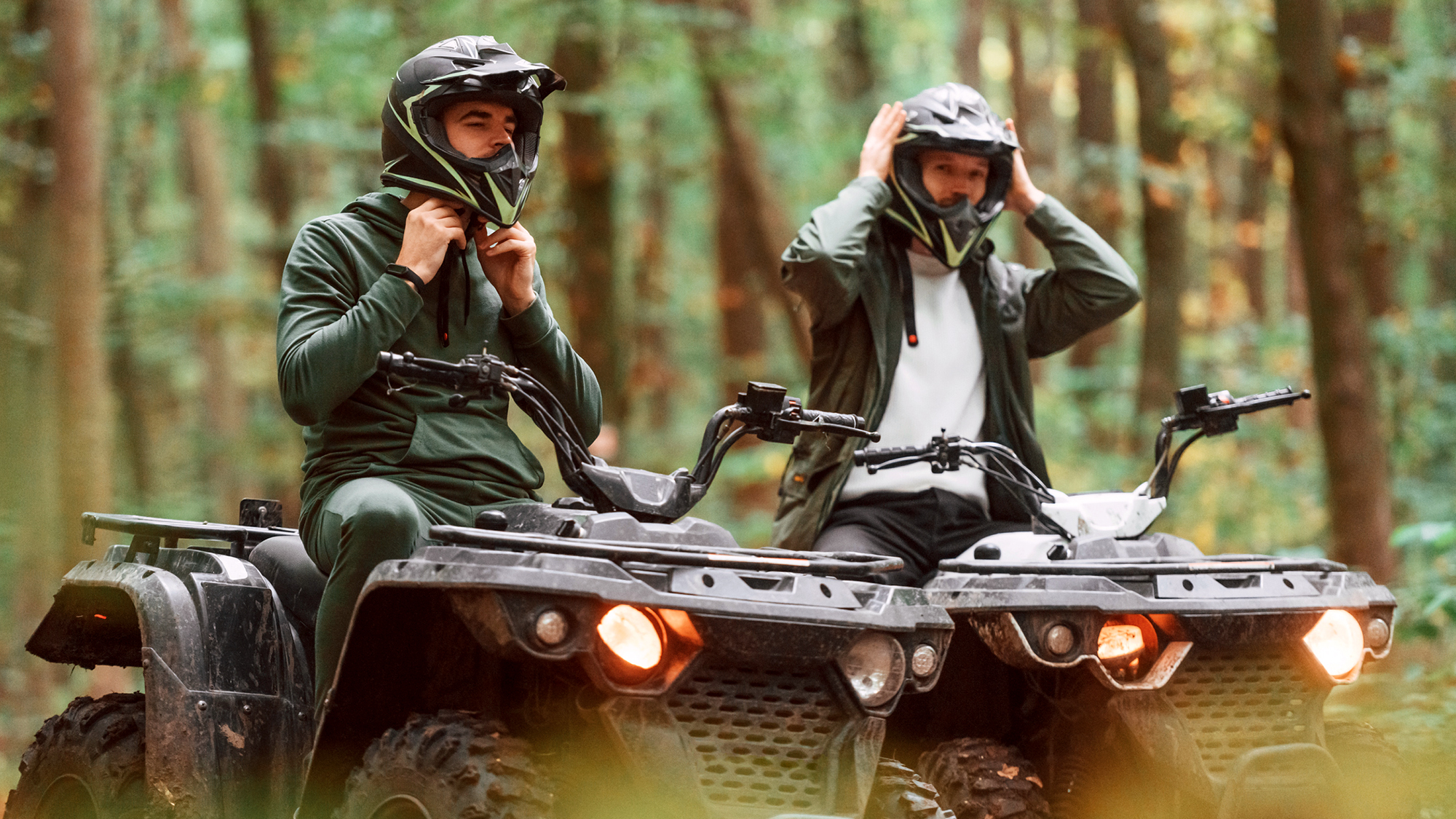 Two people on ATVs putting on helmets.