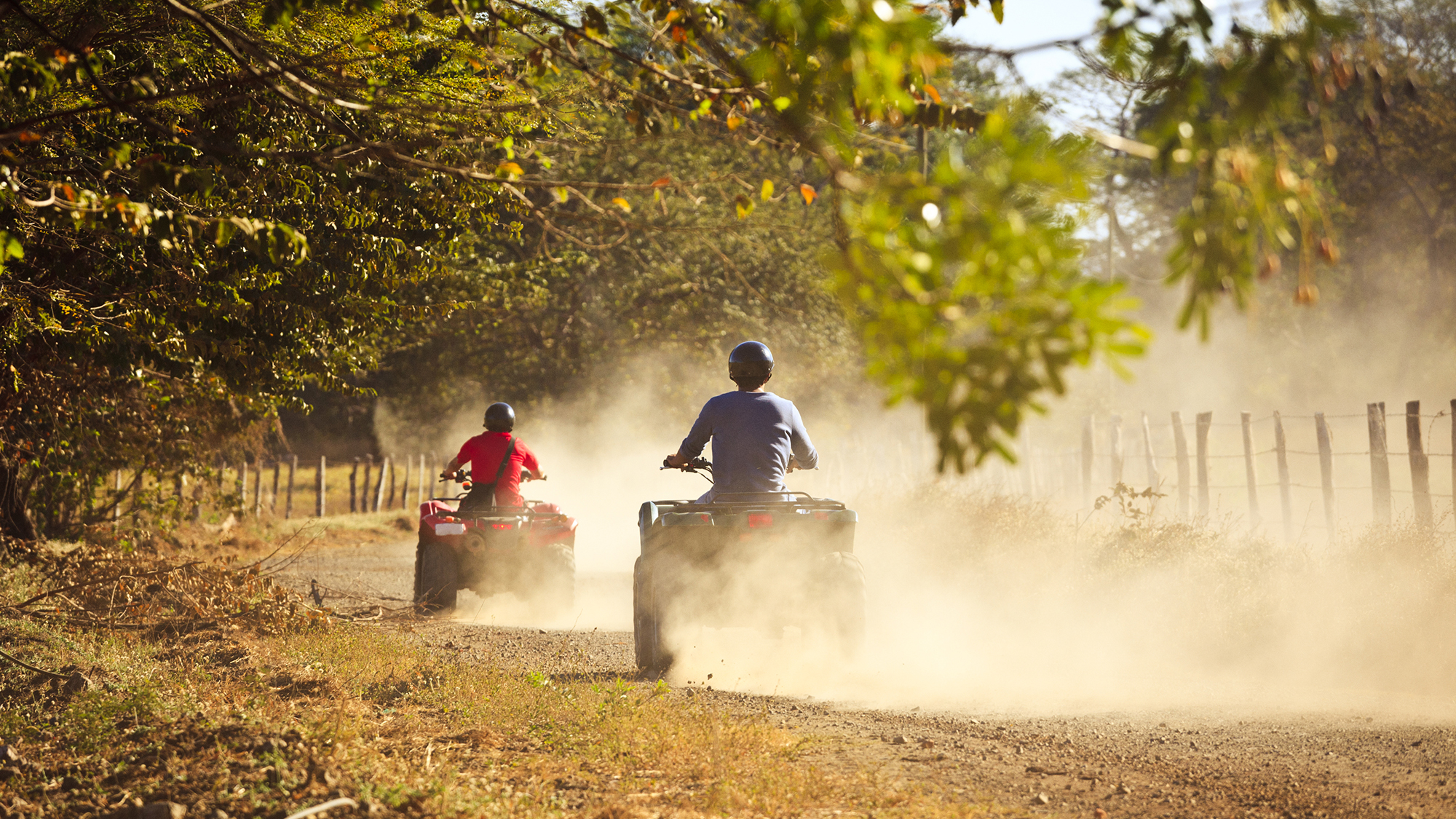 Two people riding ATVs on a dirt road.