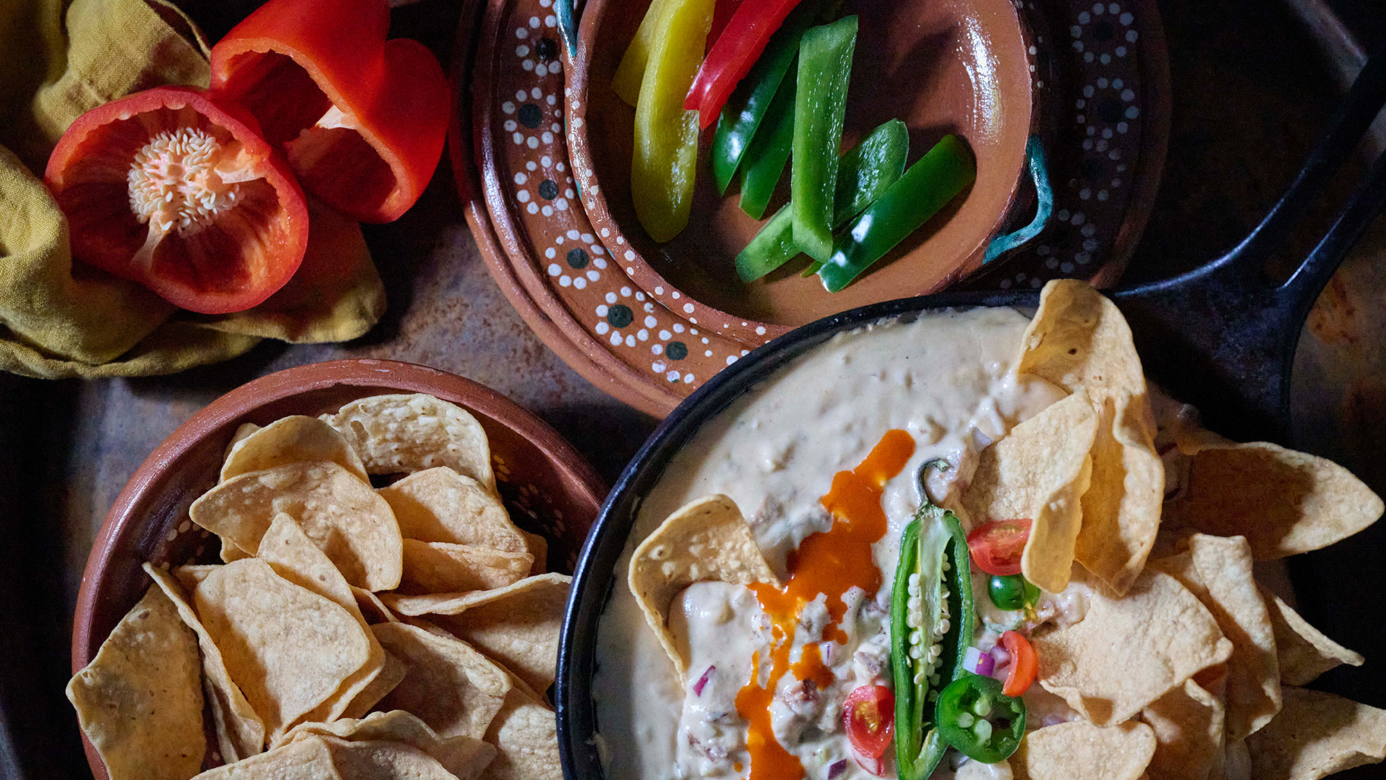 Brisket queso on a table with a side of chips and bell peppers.