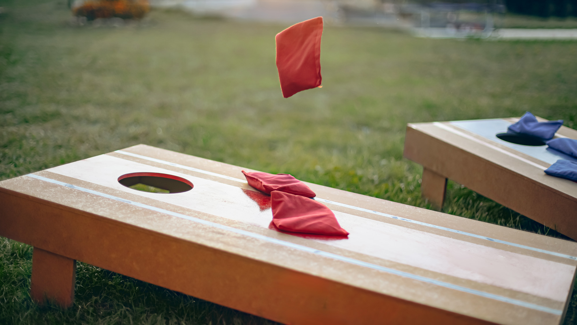 Bean bag being thrown at a corn hole board.