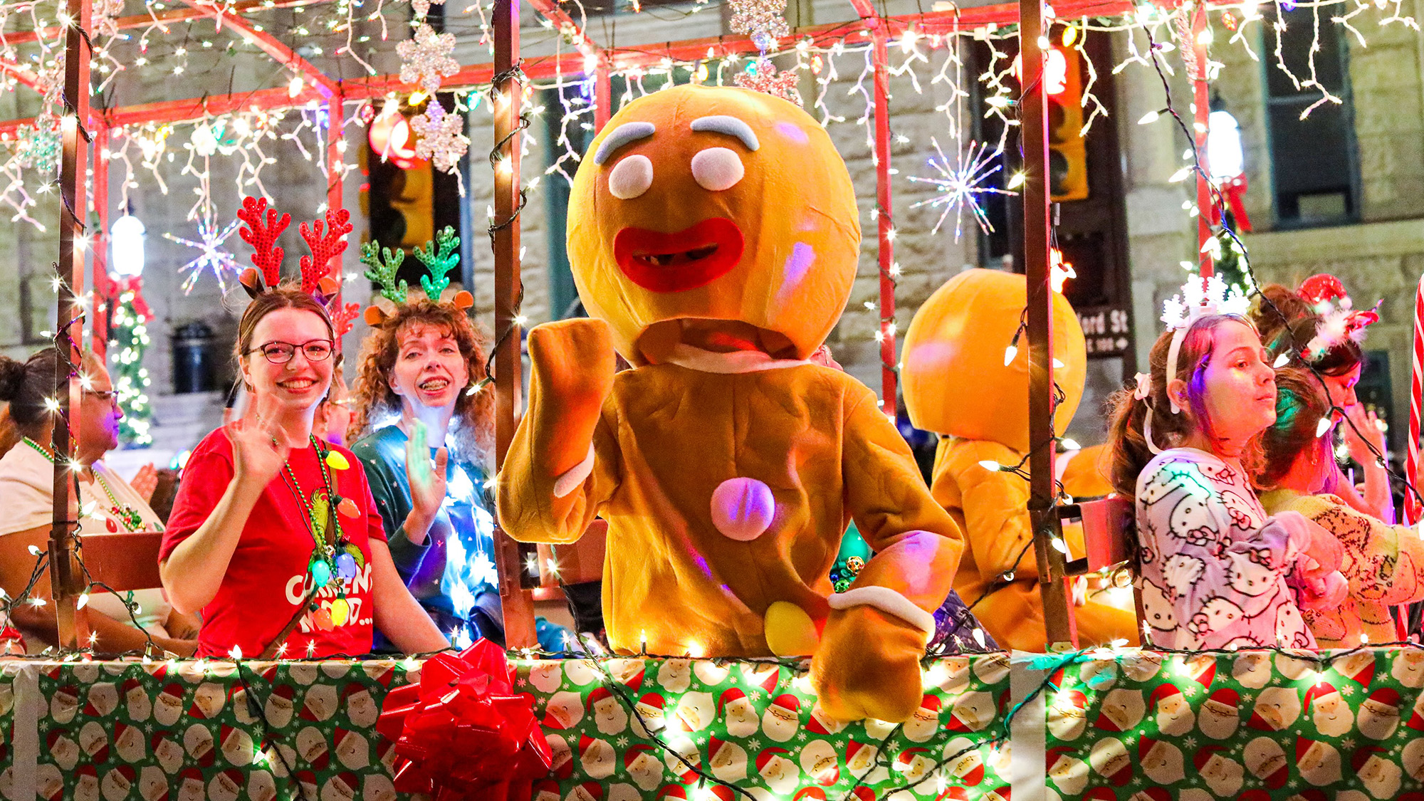 People on a holiday float with gingerbread man mascot.