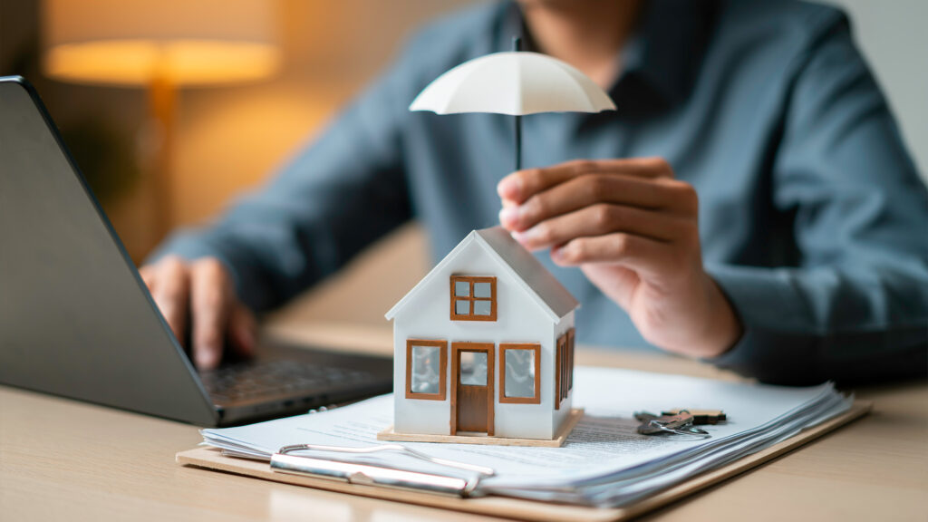 Person holding small umbrella over model home on desk.