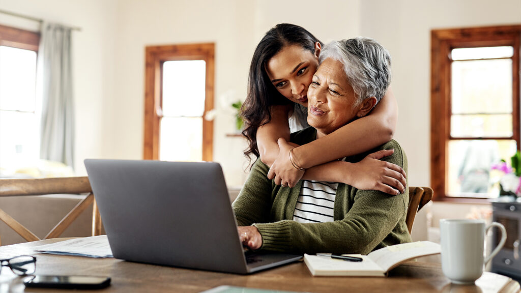 Woman hugging other older woman at computer.