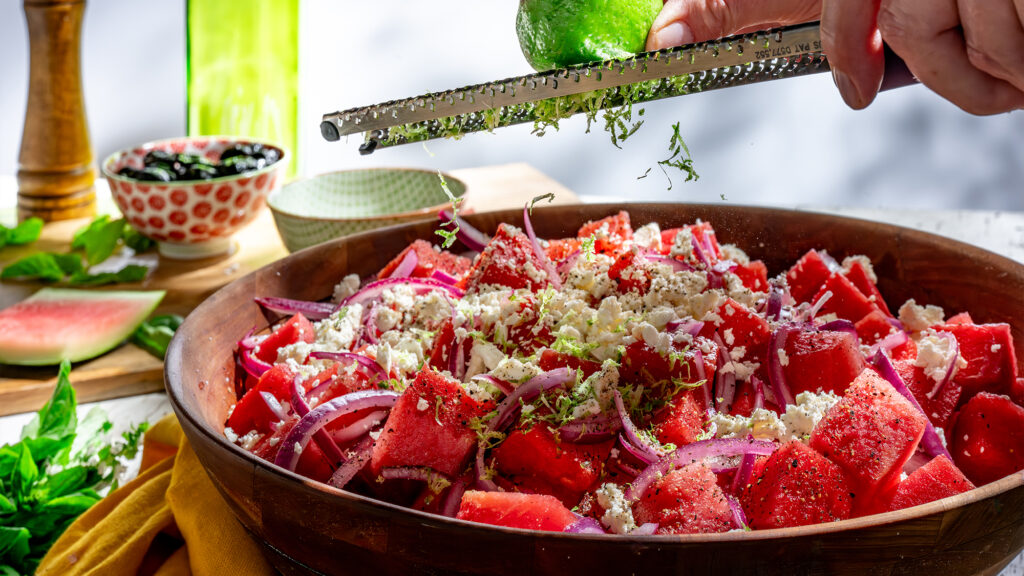 Person garnishing a watermelon salad.