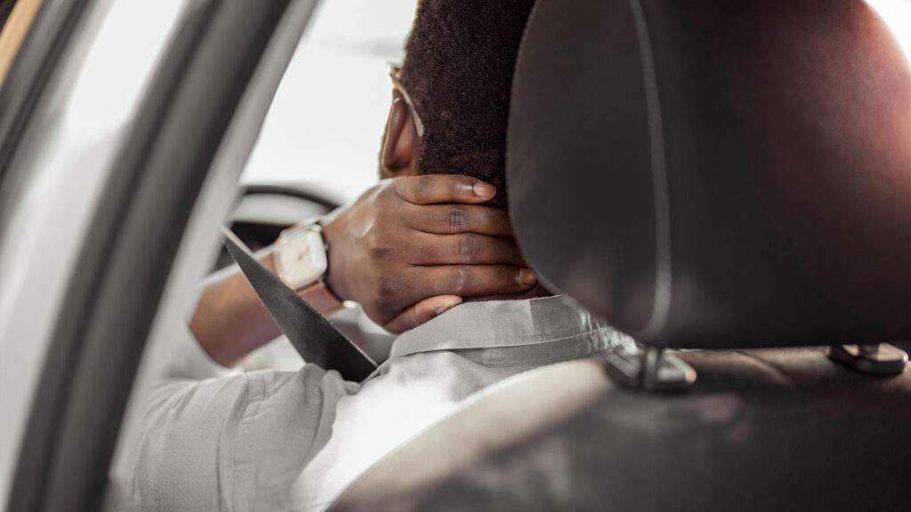 Person rubbing their neck in a driver's seat.